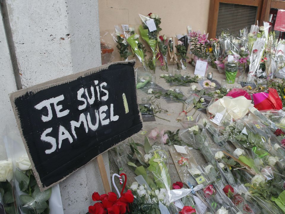A poster reading ‘I am Samuel’ and flowers lie outside the school in Conflans-Sainte-Honorine, north-west of Paris, where the murdered teacher had been working (Michel Euler/AP)