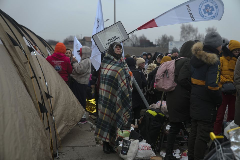 A woman warms herself with a blanket in a crowd of refugees in Poland (Markus Schreiber/AP)