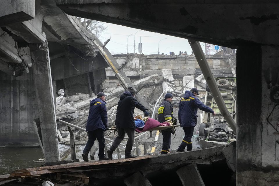 Ukrainian rescue workers carry an elderly woman under the destroyed bridge in Irpin, close to Kyiv (Efrem Lukatsky/AP)