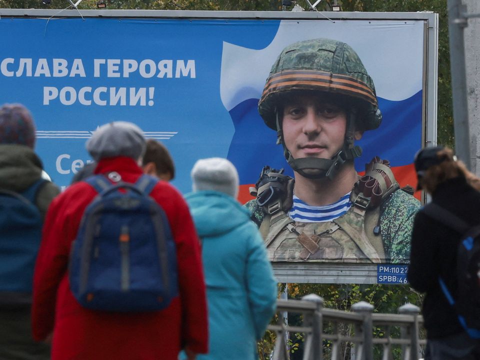 People gather at a tram stop in front of a board displaying a portrait of a Russian soldier in Saint Petersburg. Reuters