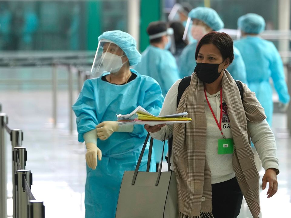 Workers wearing gowns, masks and gloves, direct arriving passengers from Manila for buses to quarantine hotels in Hong Kong international airport, Friday, April 1, 2022. Flights started landing in Hong Kong Friday after authorities lifted a COVID ban on arrivals from nine countries including Australia, Canada, France, India, Nepal, Pakistan, the Philippines, the UK and the US. (AP Photo/Kin Cheung)