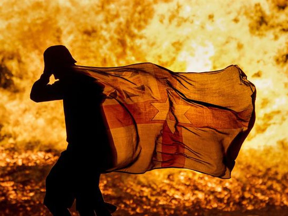 A young man carries a Northern Ireland flag in silhouette past the burning Craigyhill loyalist bonfire in Larne, Co Antrim, on the Eleventh Night (Liam McBurney/PA)
