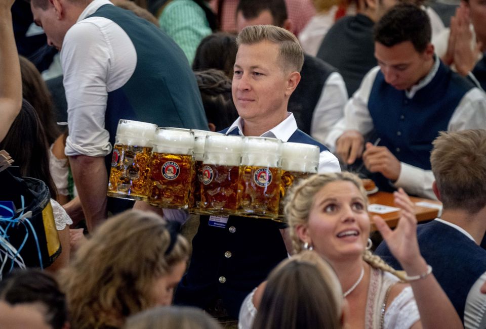 A waiter carries beer in one of the beer tents on the opening day of the 187th Oktoberfest beer festival in Munich, Germany, Saturday, Sept. 17, 2022. Oktoberfest is back in Germany after two years of pandemic cancellations, the same bicep-challenging beer mugs, fat-dripping pork knuckles, pretzels the size of dinner plates, men in leather shorts and women in cleavage-baring traditional dresses. (AP Photo/Michael Probst)