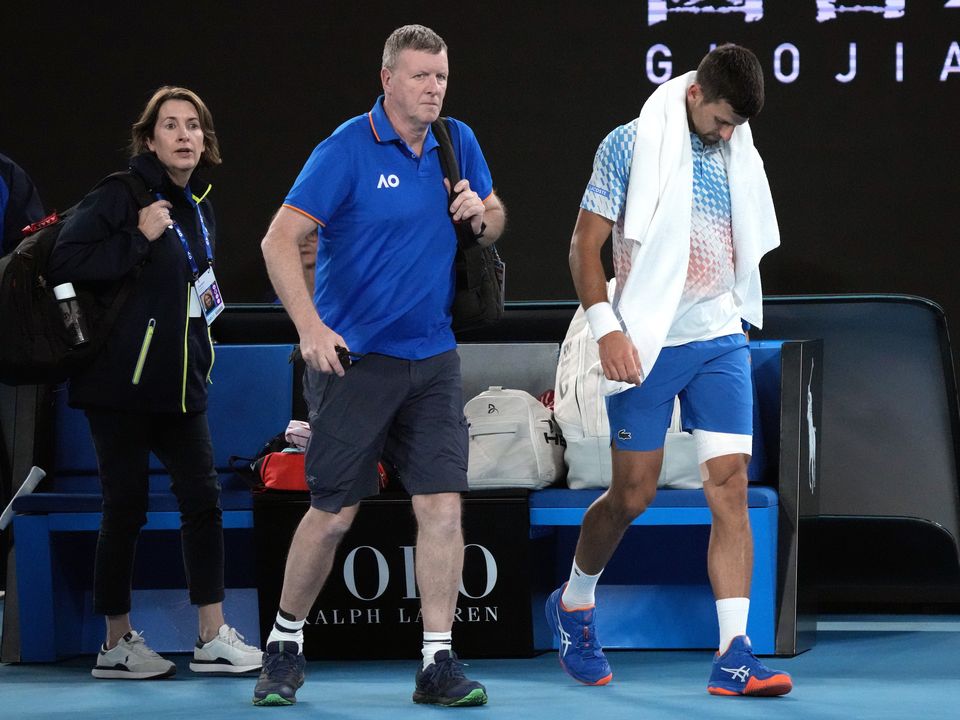Novak Djokovic, right, of Serbia leaves the court with a trainer for an injury time out during his second round match against Enzo Couacaud of France at the Australian Open tennis championship in Melbourne, Australia, Thursday, Jan. 19, 2023. (AP Photo/Dita Alangkara)