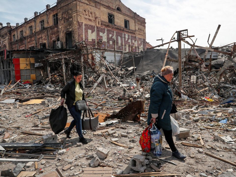 Residents carry their belongings near buildings destroyed in Mariupol