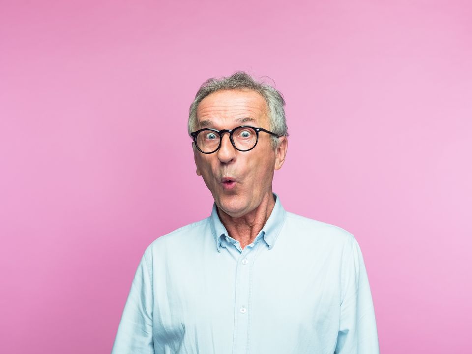 Portrait of shocked retired elderly man making face over pink background