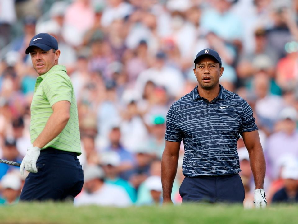 Tiger Woods walks from the first tee as Rory McIlroy looks on