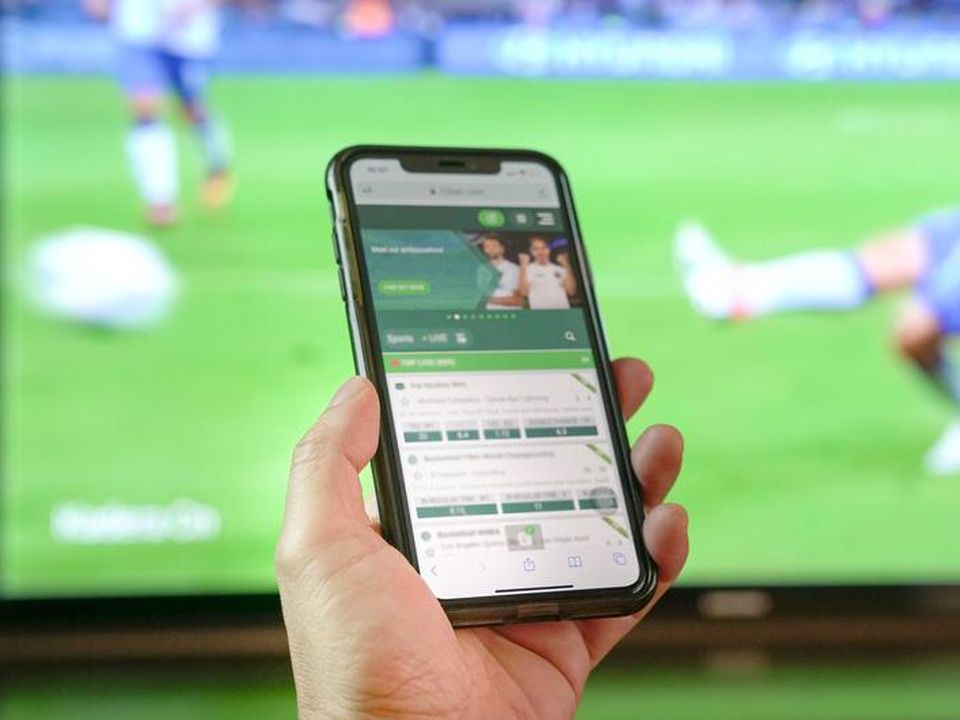 Person watching football match on TV and making bets on bookmakers app (stock)