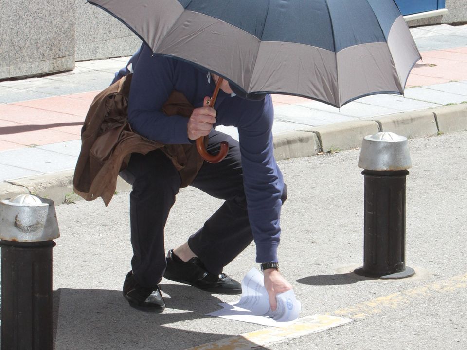 Kinahan Snr stumbles and drops documents as he emerges from court, using an umbrella as a shield