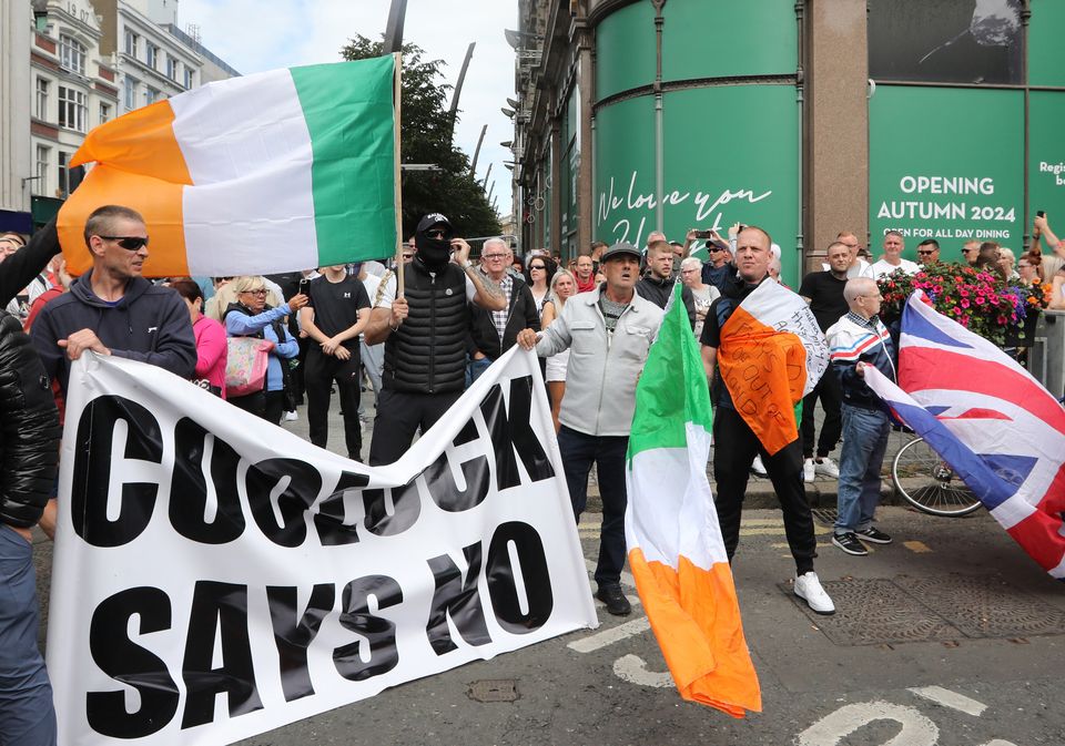 ‘Coolock Says No’ flag with Loyalist protesters on the streets of Belfast