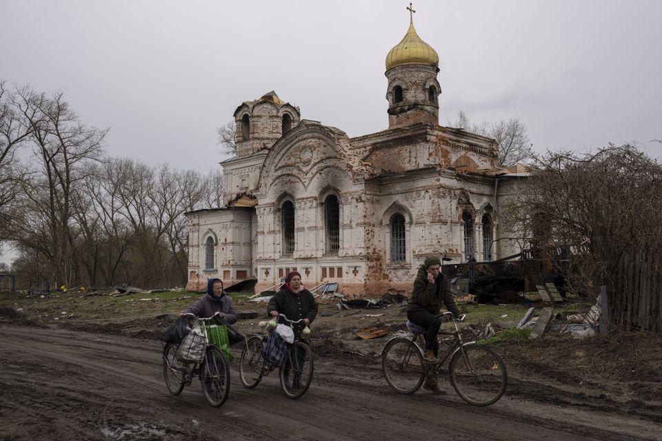 Residents walk with their bicycles in front of a damaged church in Lukashivka, northern Ukraine (Petros Giannakouris/AP)