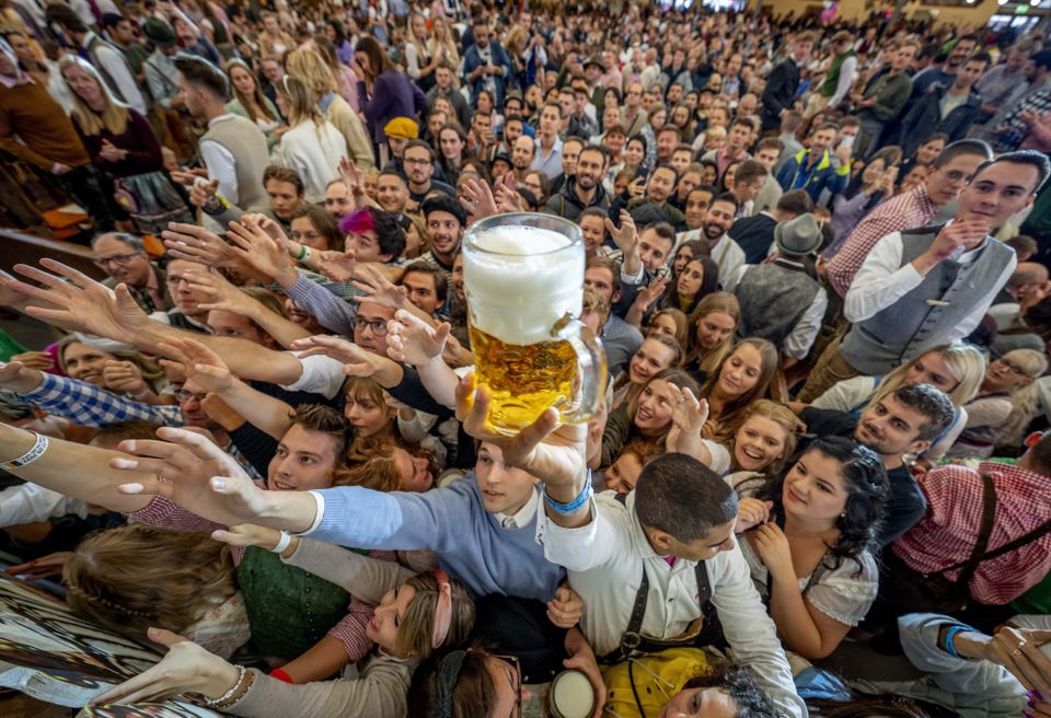 Young people reach out for free beer in one of the beer tents on the opening day of the 187th Oktoberfest beer festival in Munich, Germany, Saturday, Sept. 17, 2022. Oktoberfest is back in Germany after two years of pandemic cancellations, the same bicep-challenging beer mugs, fat-dripping pork knuckles, pretzels the size of dinner plates, men in leather shorts and women in cleavage-baring traditional dresses. (AP Photo/Michael Probst)