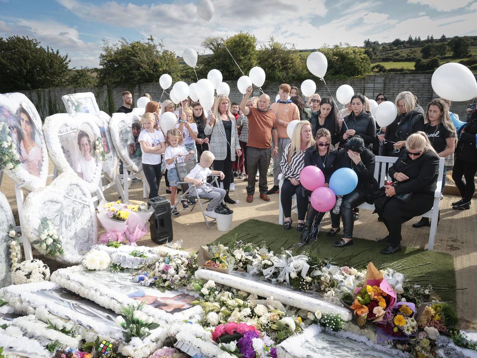 The children’s mother Margaret sits by their graves, comforted by friends and family
