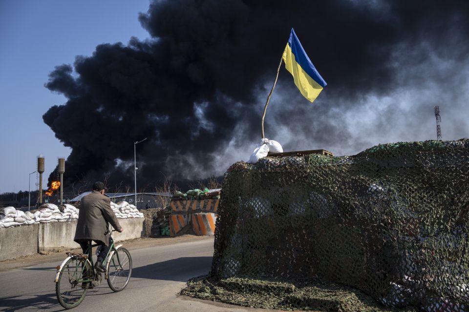 A man rides a bicycle as black smoke rises from a fuel storage tank following a Russian attack on the outskirts of Kyiv (Rodrigo Abd/AP)