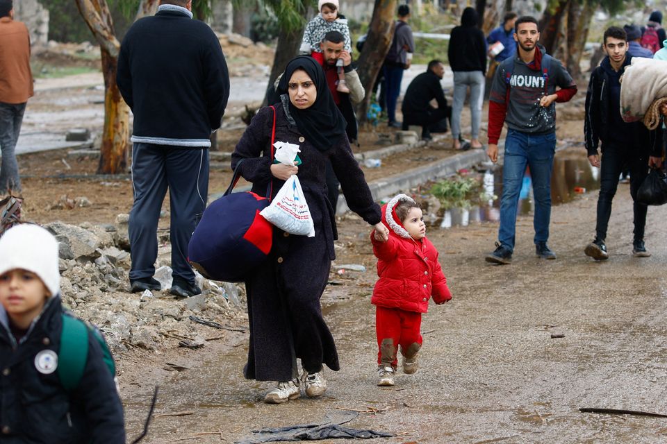 A woman walks with a child, as Palestinians fleeing north Gaza move southward during a temporary truce between Israel and Hamas, near Gaza City, November 27, 2023. REUTERS/Ibraheem Abu Mustafa.