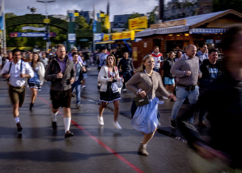 Visitors run onto the festival ground on the opening day of the 187th Oktoberfest beer festival in Munich, Germany, Saturday, Sept. 17, 2022. Oktoberfest is back in Germany after two years of pandemic cancellation, the same bicep-challenging beer mugs, fat-dripping pork knuckles, pretzels the size of dinner plates, men in leather shorts and women in cleavage-baring traditional dresses. (AP Photo/Michael Probst)